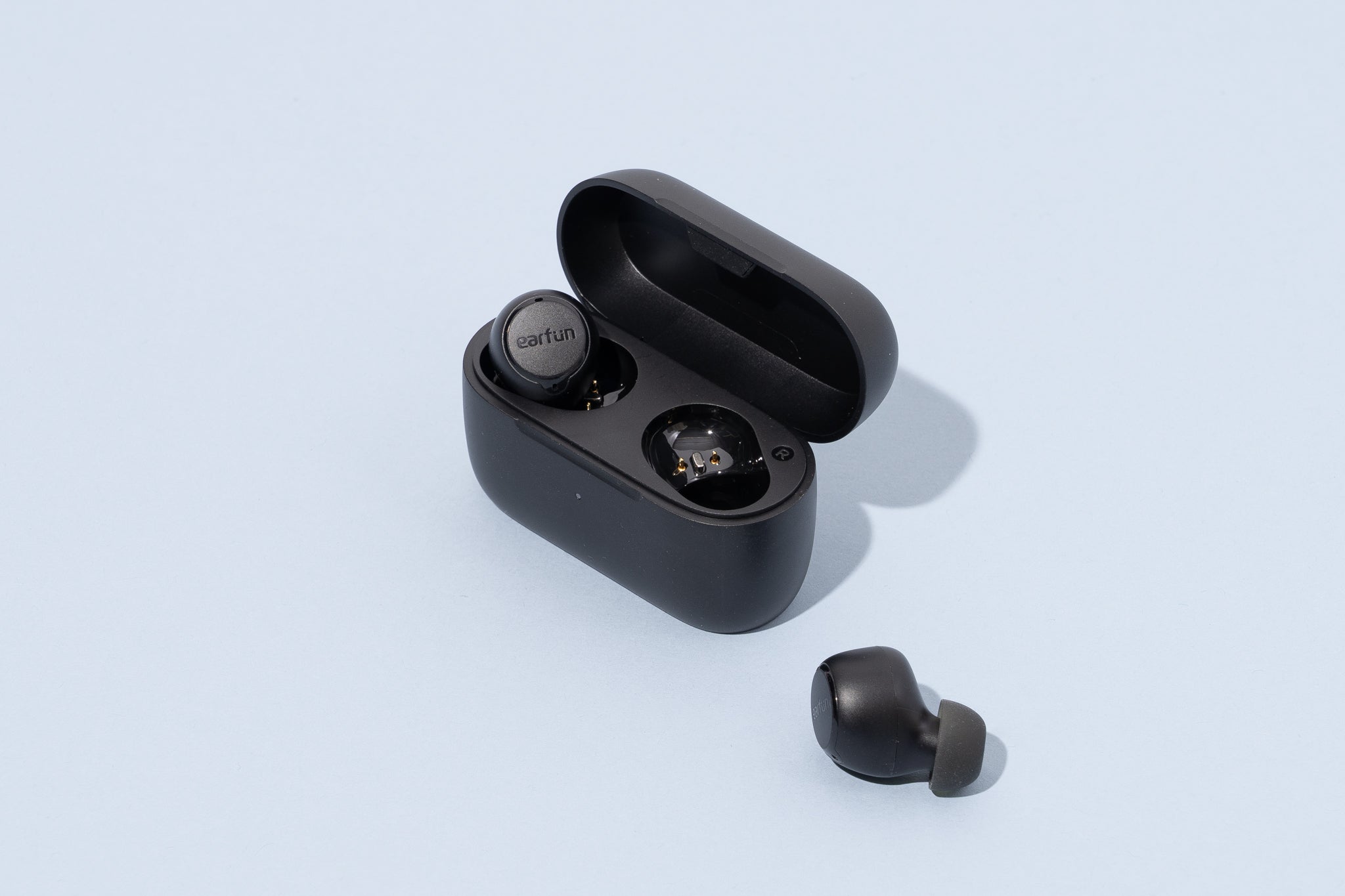 The EarFun Free 2S earbuds sit with one earbud in the case, and one next to it.